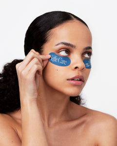 Woman applying eye patches with 'The Cure' branding on a white background